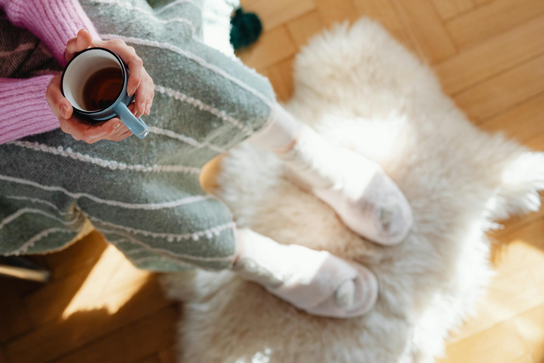 A person in cozy socks holding a warm drink on a soft rug