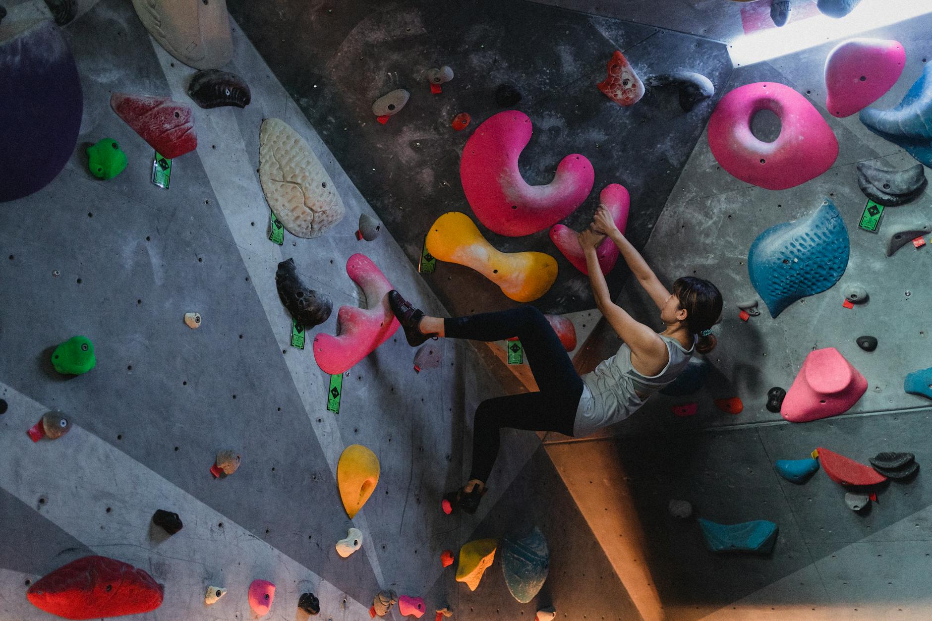A climber on an indoor bouldering wall with colorful grips