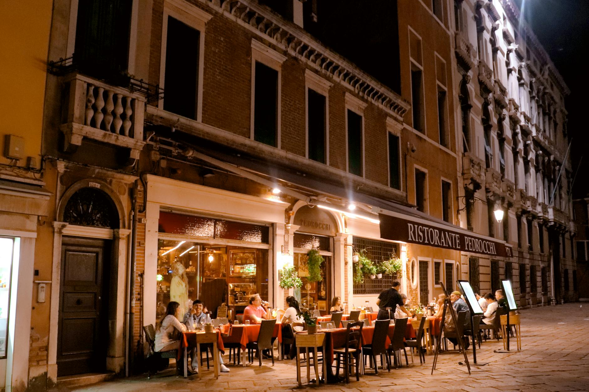 Diners enjoying a meal at outdoor restaurant tables in the evening