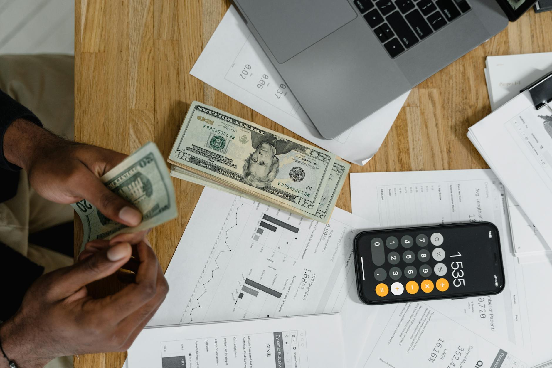 Hands with a calculator, charts, and cash on a desk
