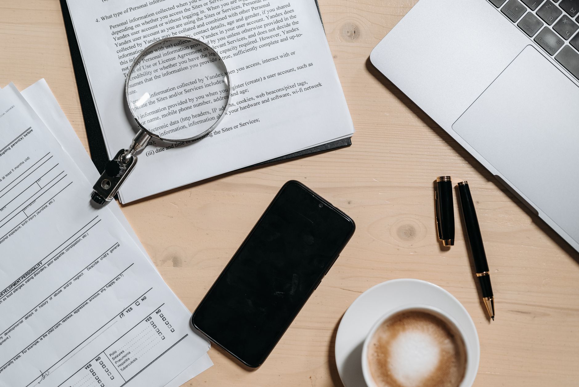 Documents, a laptop, coffee, and a magnifying glass on a desk