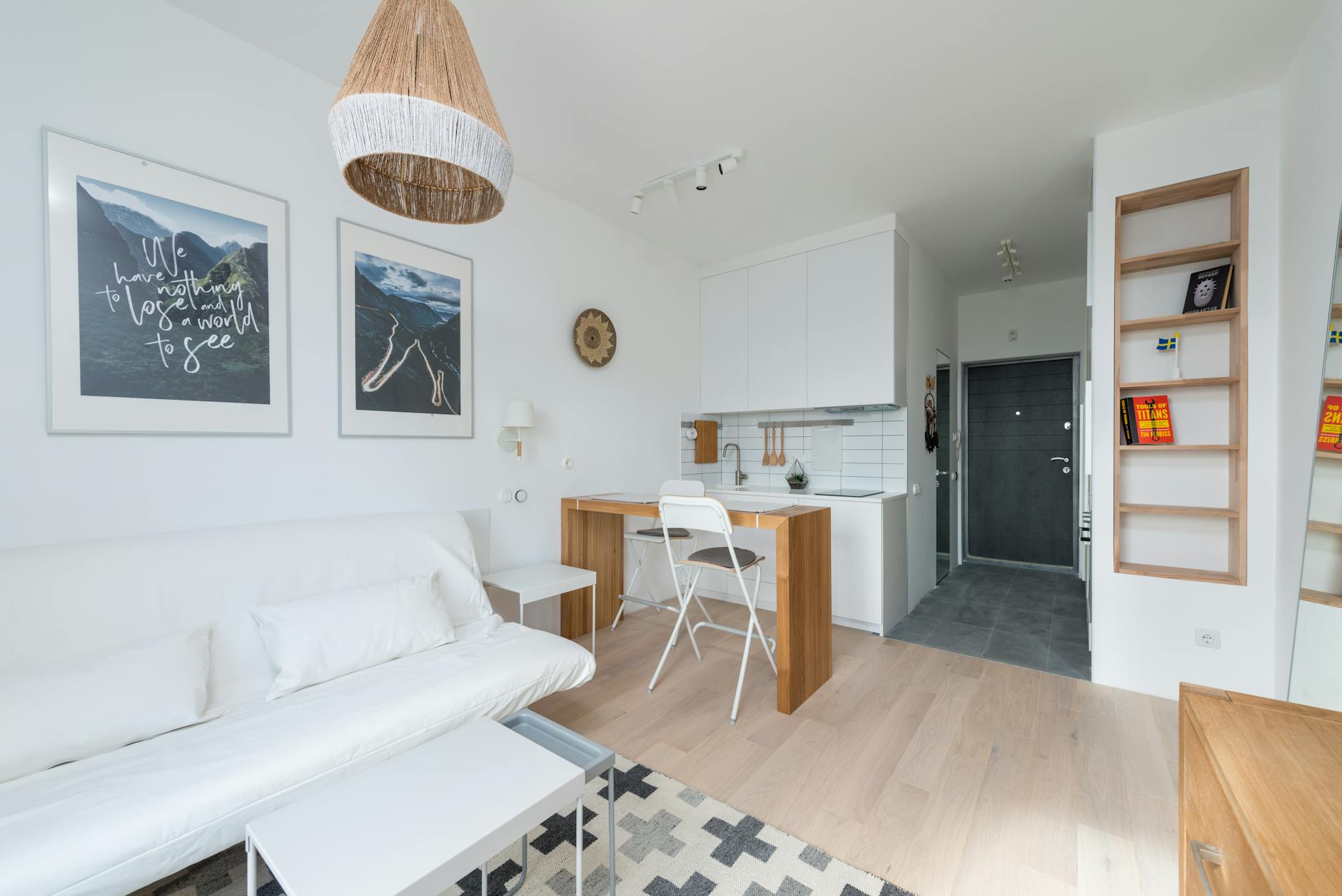 A bright, minimalist studio apartment with a white sofa and wood furniture