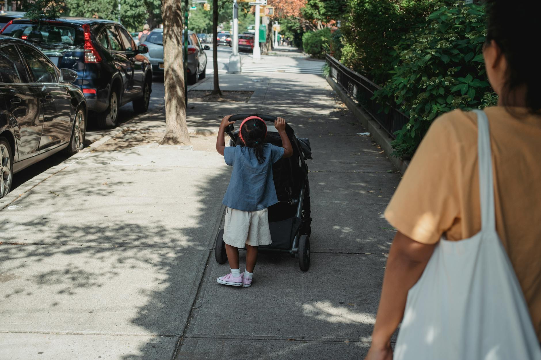 A parent walking on a sunny pathway with a child and a baby stroller