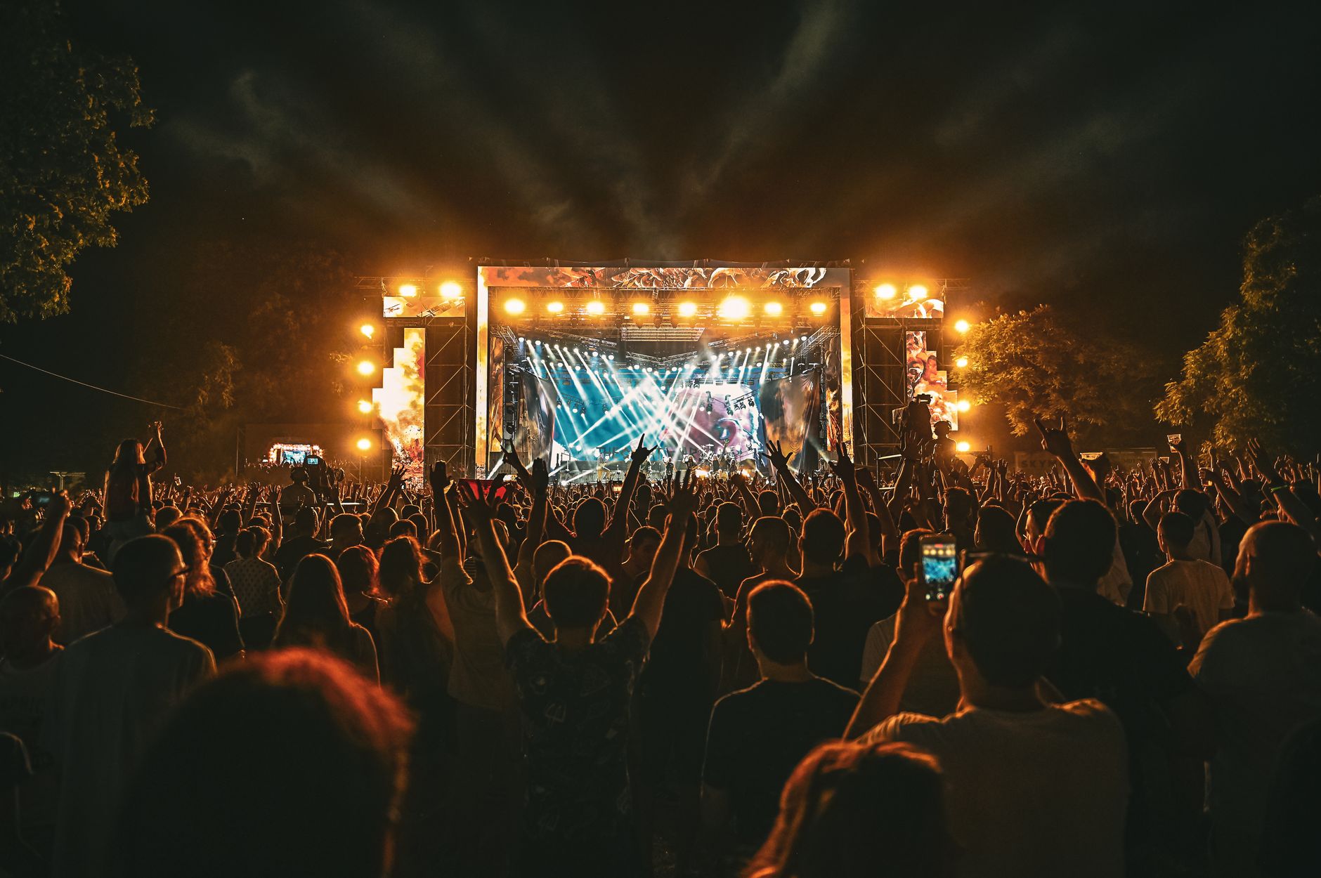A large crowd at an outdoor concert at night with stage lighting