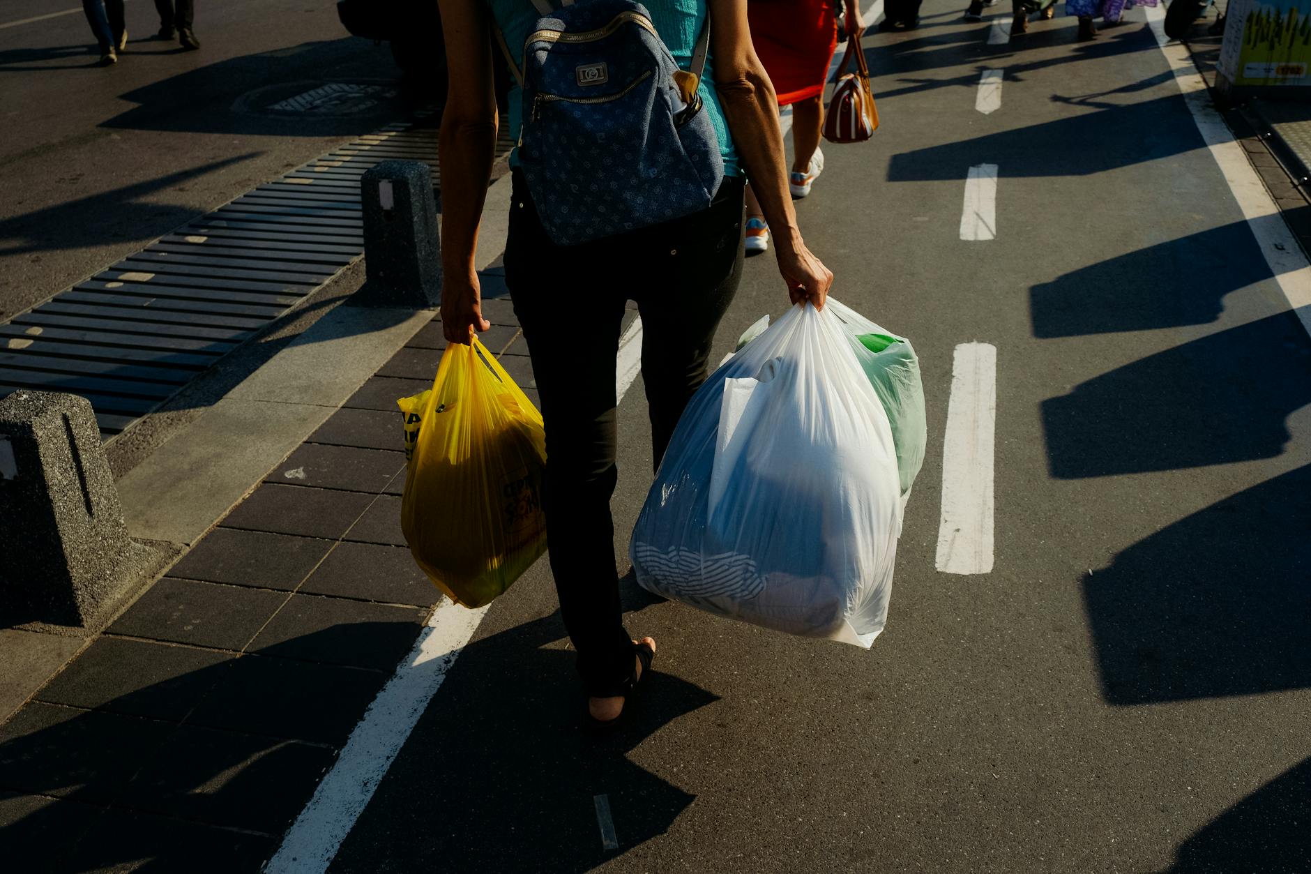 A person walking on a sidewalk carrying grocery bags on a sunny day